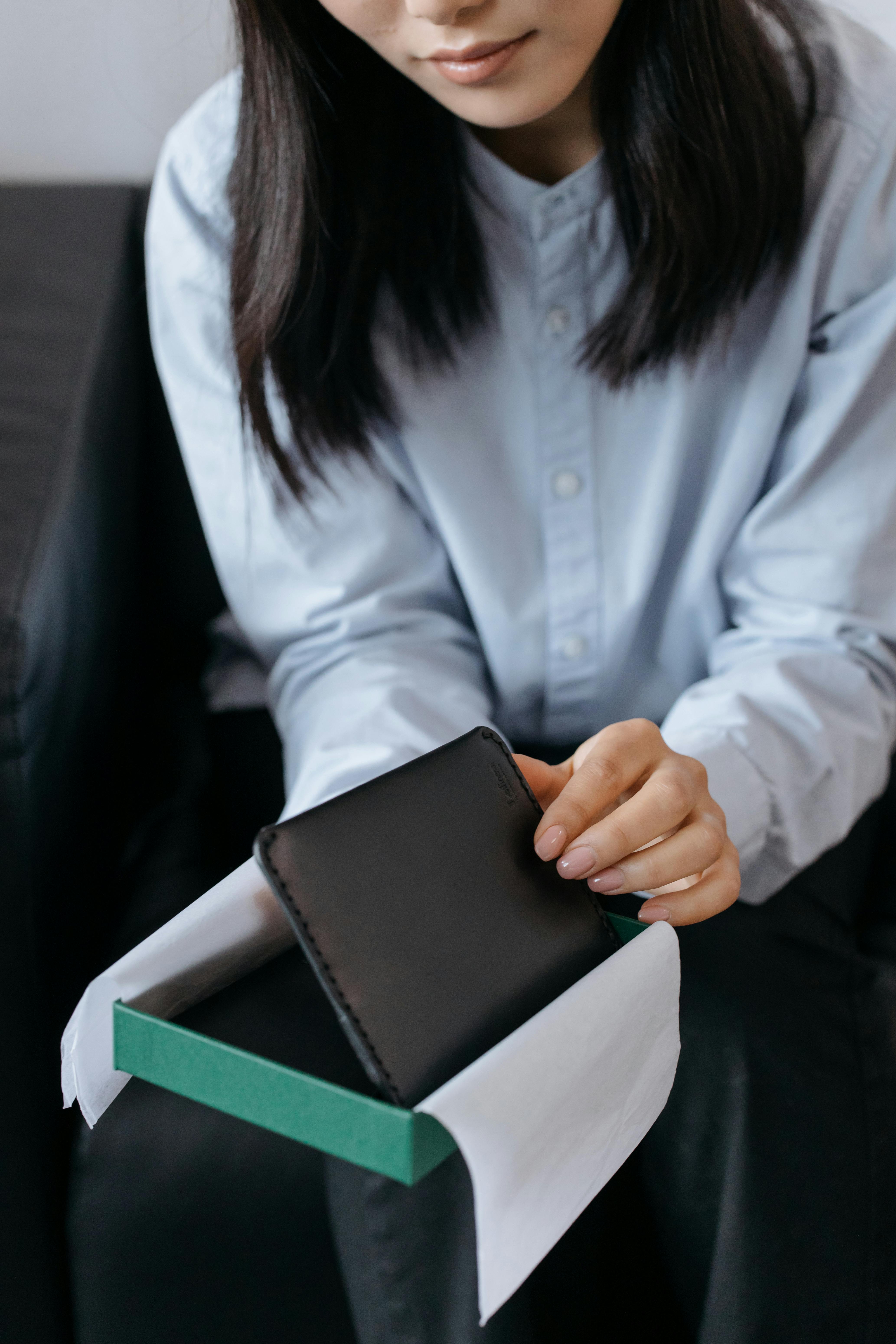 A woman opens a gift box containing a sleek black leather wallet, showcasing minimalist style and elegance.