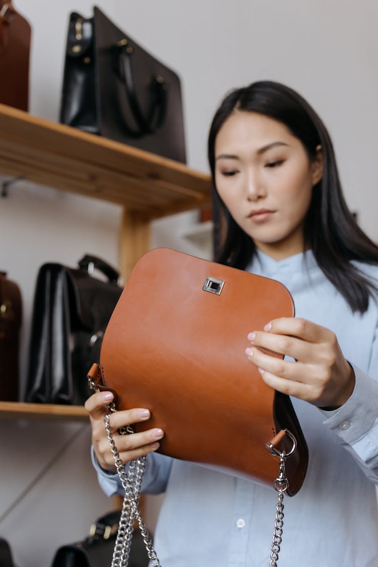 A Pretty Woman Holding A Brown Leather Shoulder Bag With A Chain Strap