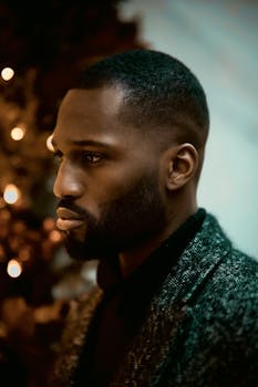 Portrait of a well-dressed man with a beard, highlighted by warm festive lights.