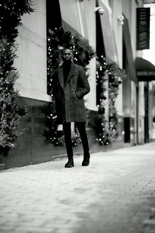 Grayscale Photo of a Man Walking Near a Building with Christmas Decors