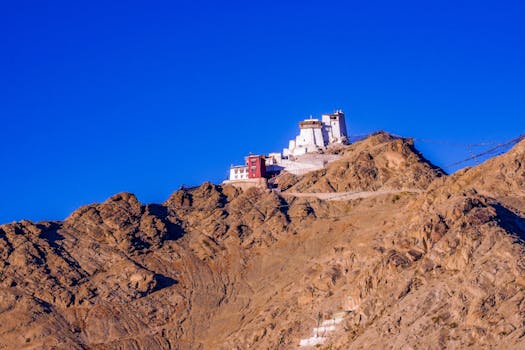 Scenic view of a monastery perched on a rocky mountain under a clear blue sky.