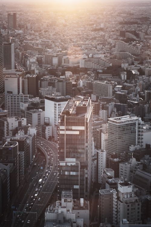 Free Drone view of asphalt road between multistory buildings and skyscrapers of Tokyo against sunset sky Stock Photo