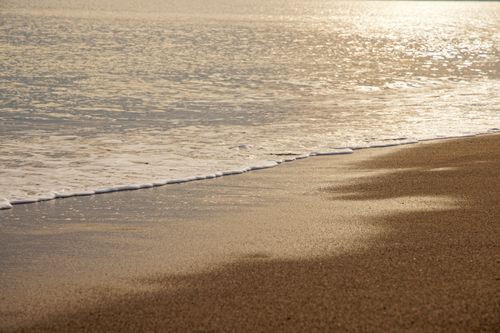 Free Tranquil beach scene with calm waves gently lapping over the sandy shore during sunset. Stock Photo