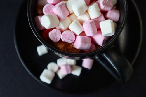 Free Warm black mug filled with hot chocolate and colorful marshmallows on a dark surface. Stock Photo