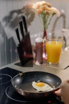 Fried egg cooking in a non-stick pan on an induction stove with a knife set and orange juice in the background.