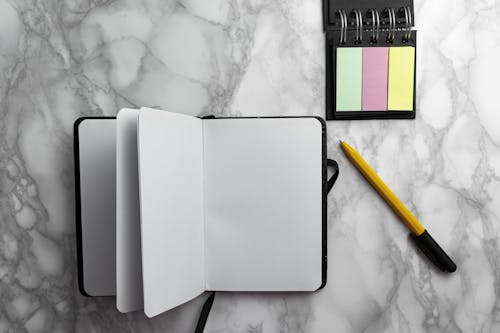 A Blank Notebook and Sticky Notes on Marble Surface