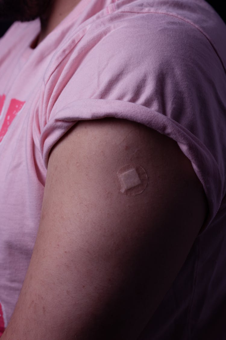 A Person In Pink Shirt With Round Band Aid On Arm