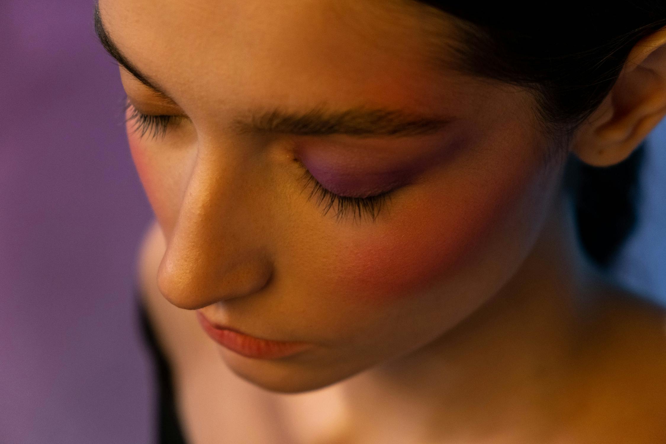 A woman applying contour makeup on her cheekbones with a brush.