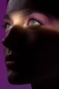Close-up portrait of a woman with purple eye shadow and mysterious lighting.