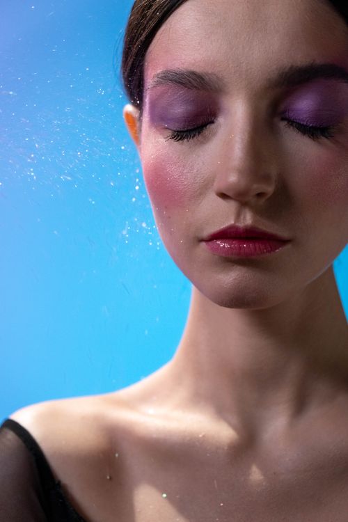 Free Close-up of a woman with colorful makeup on a blue background, eyes closed. Stock Photo