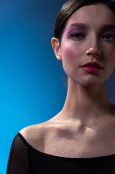 Close-up portrait of a woman with shimmering makeup on a blue background, exuding elegance and style.