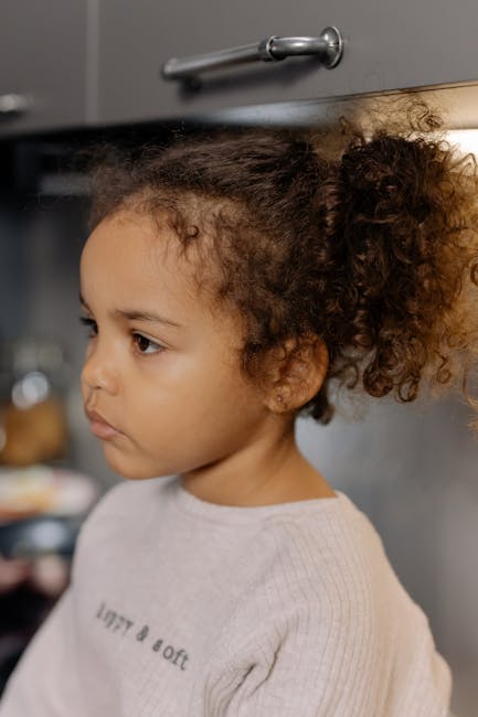Side view of a young girl with curly hair looking contemplative indoors.