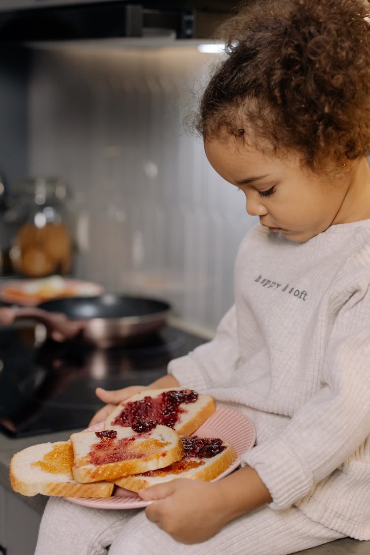 A Girl In Pajama Holding A Plate Of  Sandwiches With Strawberry Jam