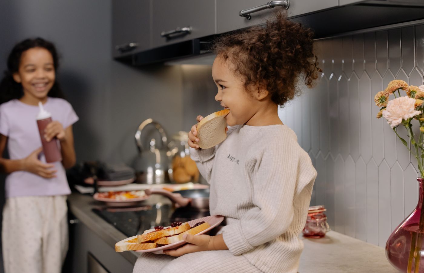 Two children having breakfast in a modern kitchen, enjoying sandwiches and laughter.