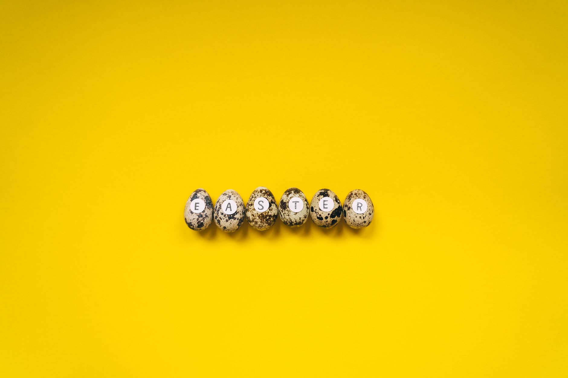 Quail eggs with letters spelling Easter on a bright yellow background, minimalist style.
