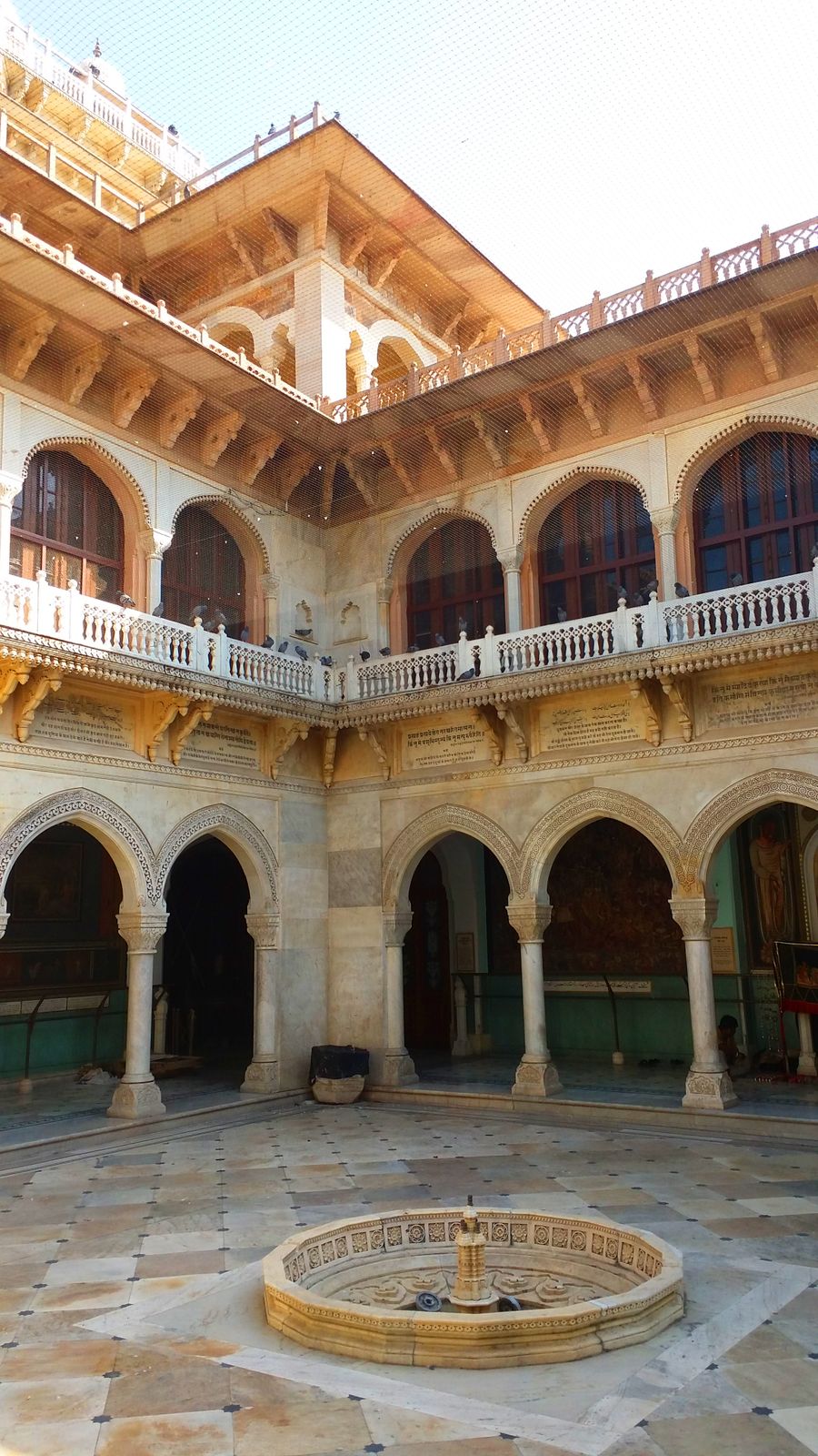 A marble courtyard ringed with two tiers of carved arches and a balustraded gallery.