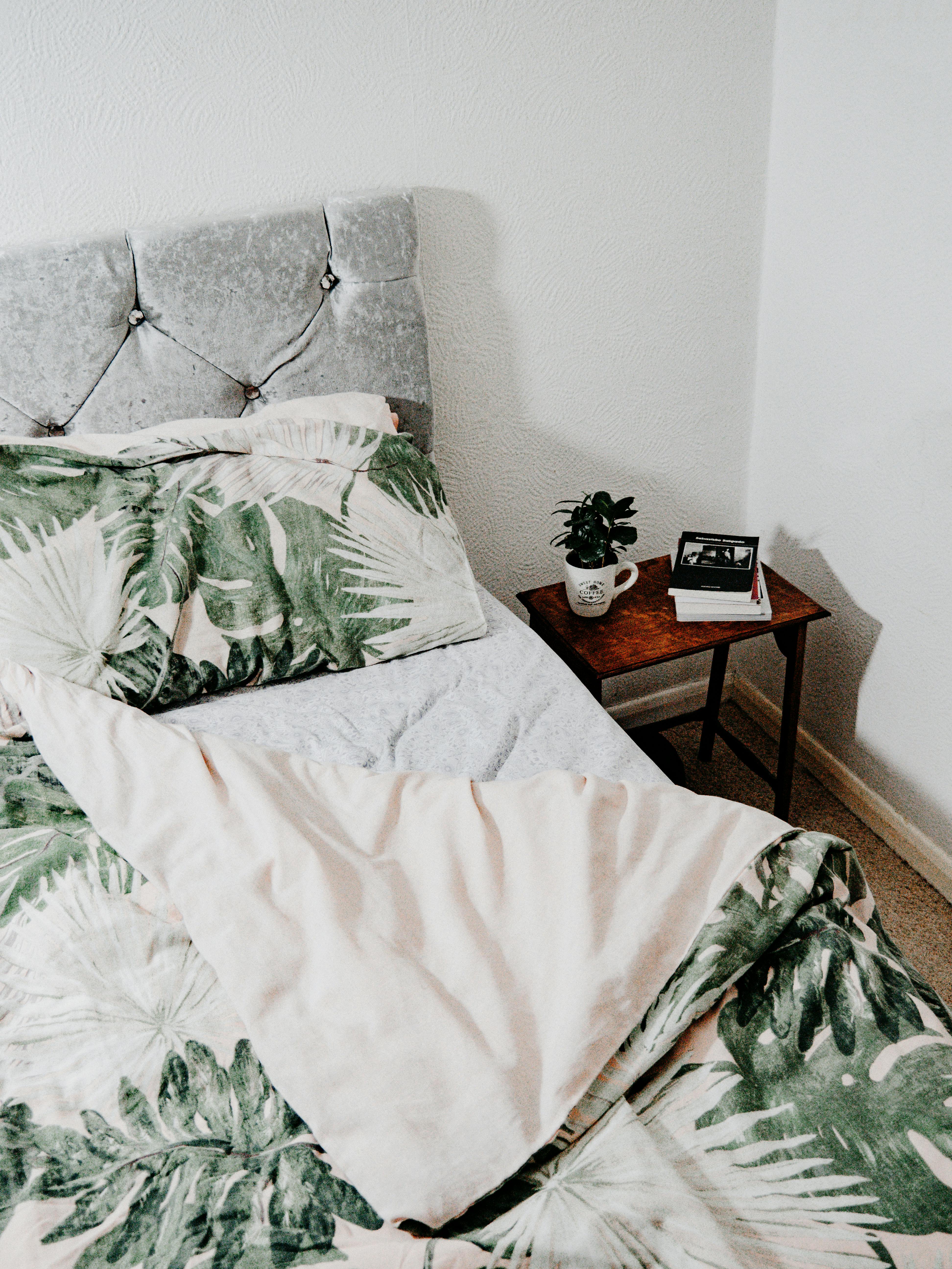 Free Inviting bedroom featuring tropical leaf bedding and cozy interior design. Stock Photo