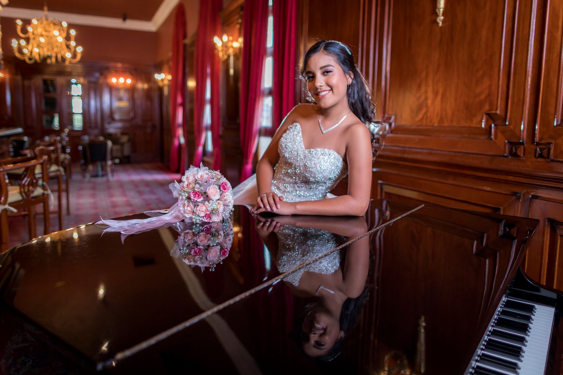 Smiling woman in elegant gown with bouquet, posing by a grand piano in a luxurious room.