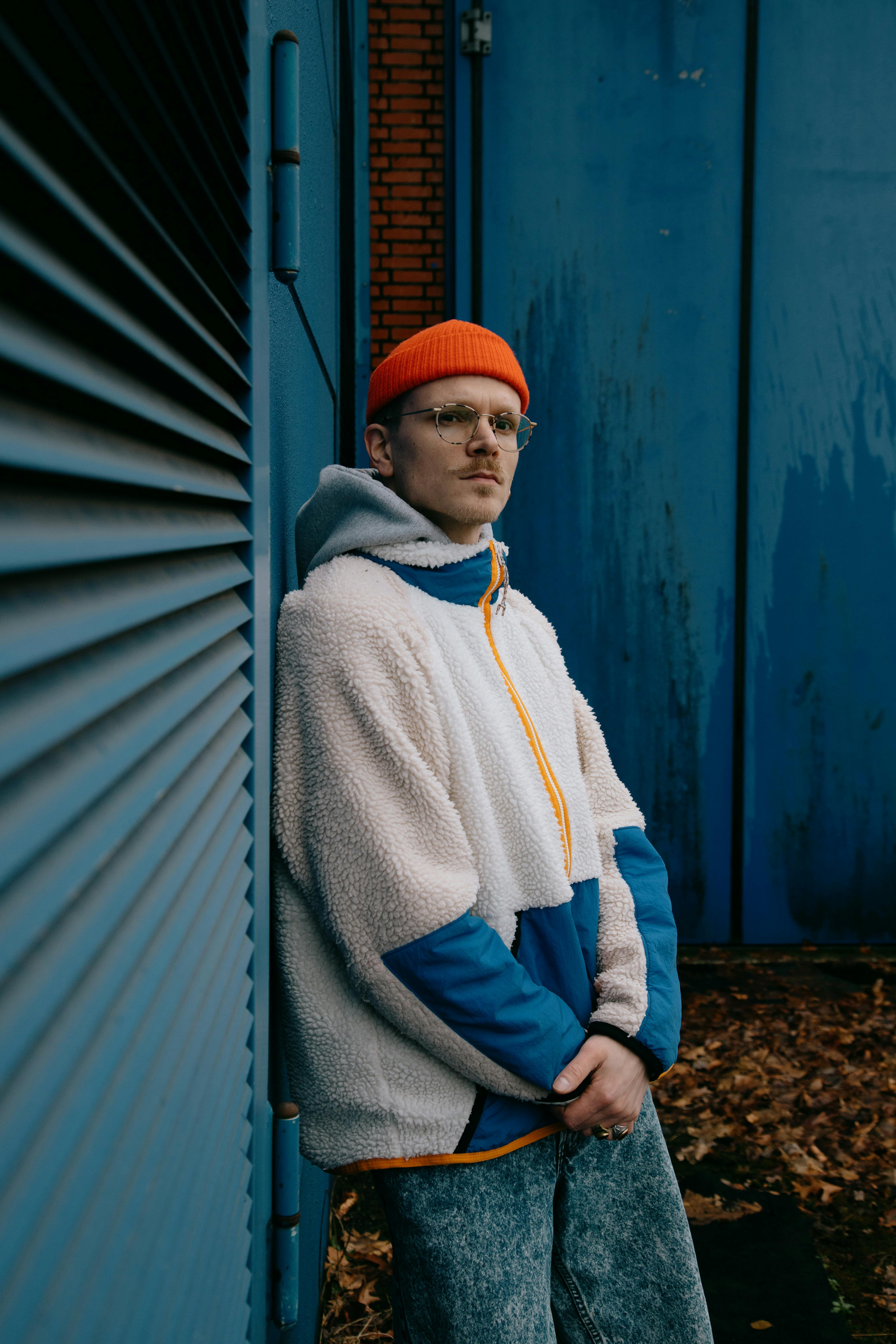 Young man in stylish outfit leaning against a blue wall in an urban environment.