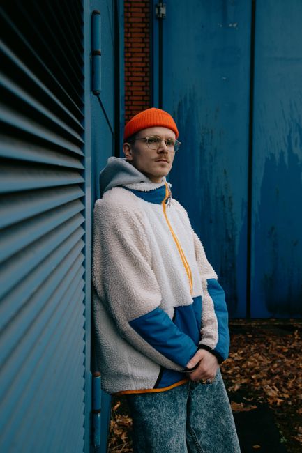 Young man in stylish outfit leaning against a blue wall in an urban environment.