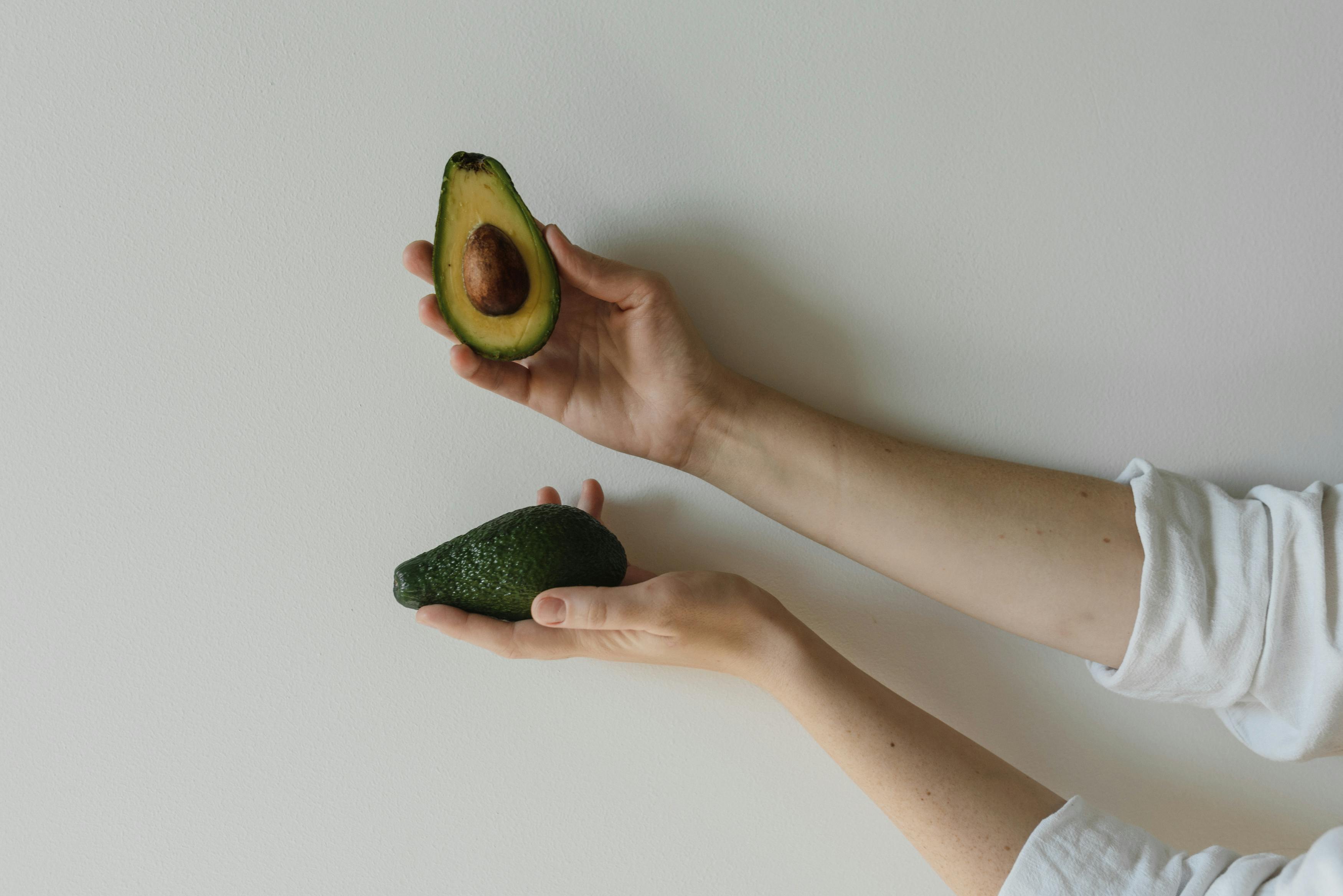 Hands holding a whole and a sliced avocado, emphasizing its skin-friendly nutrients.