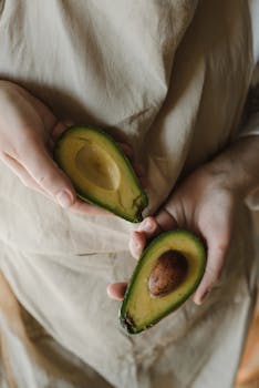 Close-up of hands holding sliced avocado, showcasing freshness and organic appeal.