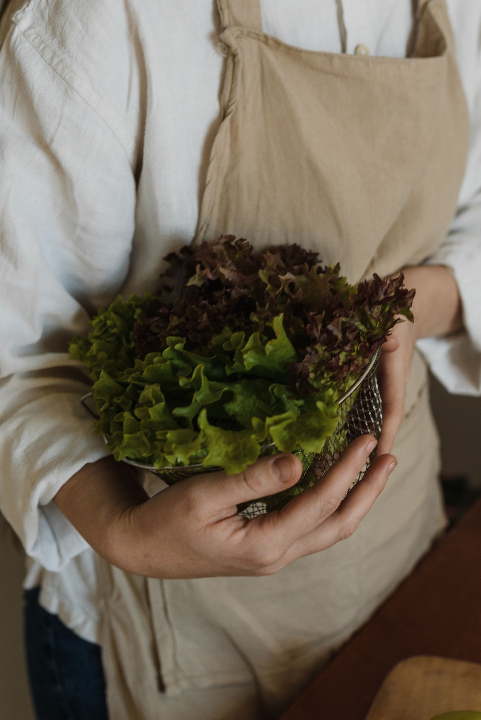 Person washing and holding fresh lettuce leaves over a metal strainer in a kitchen, illustrating the greens-washing step before spinning