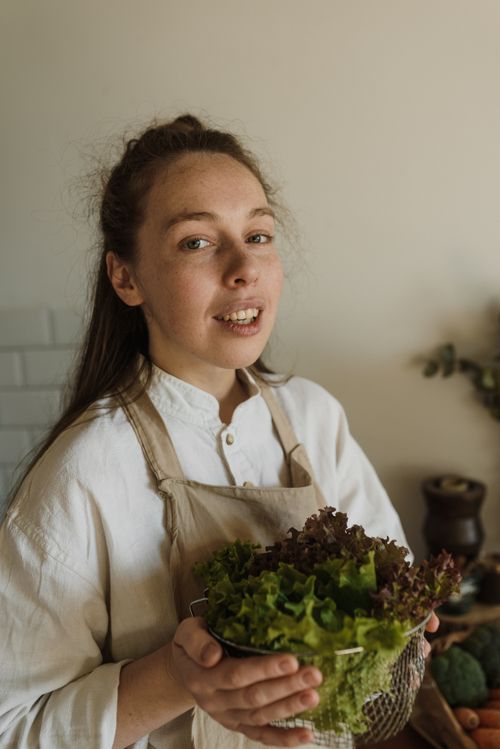 Free Young woman holding a colander of fresh lettuce in a cozy indoor setting. Stock Photo