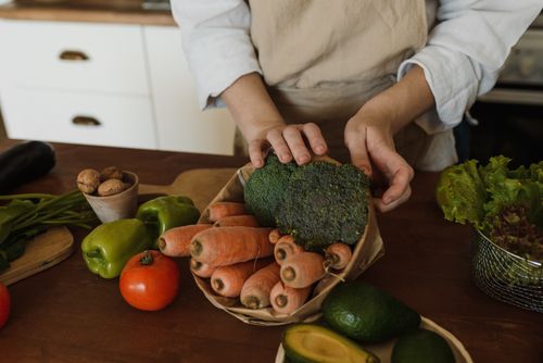 Free Hands arranging fresh broccoli and carrots with other vegetables on a kitchen counter. Stock Photo