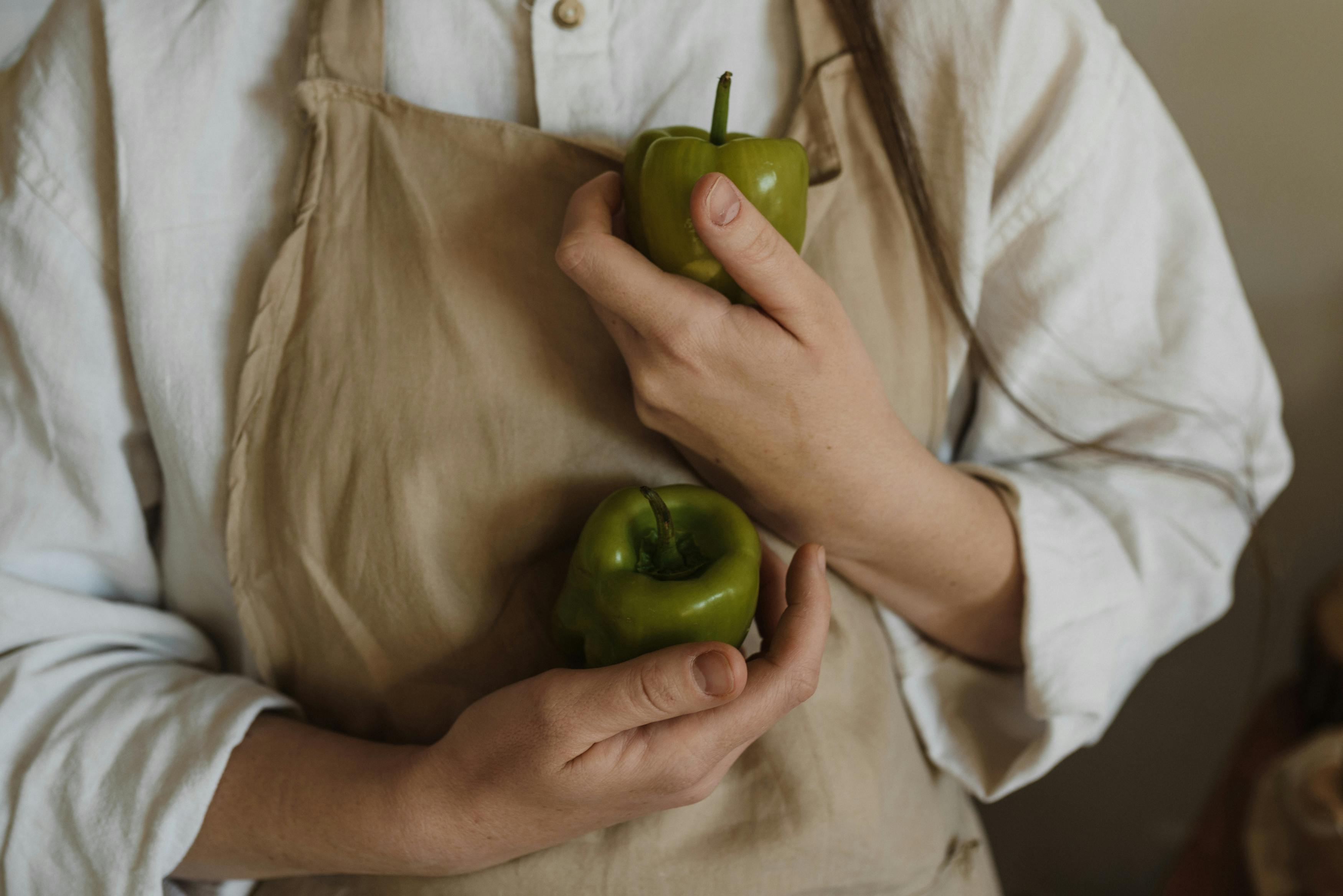 a person with beige apron holding green bell peppers