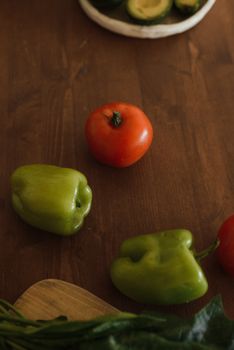 A vibrant display of green bell peppers and a ripe tomato on a wooden kitchen surface in natural light.