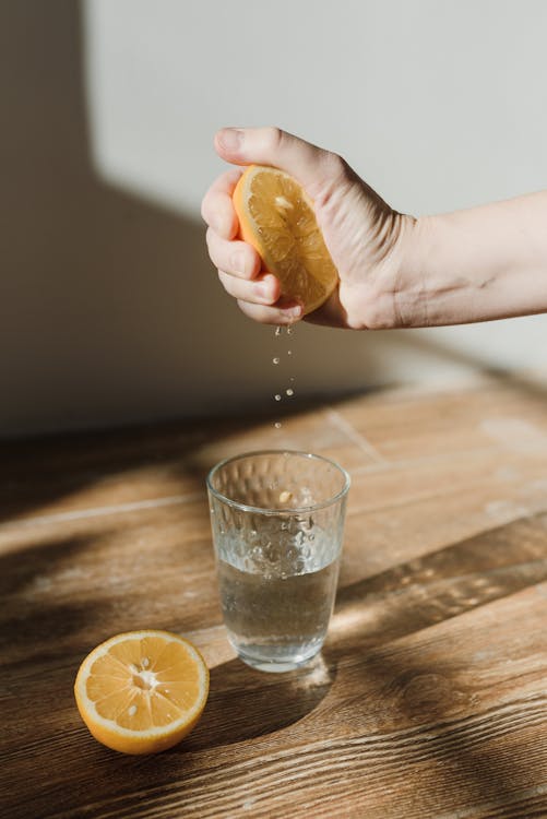 Free A Person Squeezing a Lemon in a Glass of Water Stock Photo