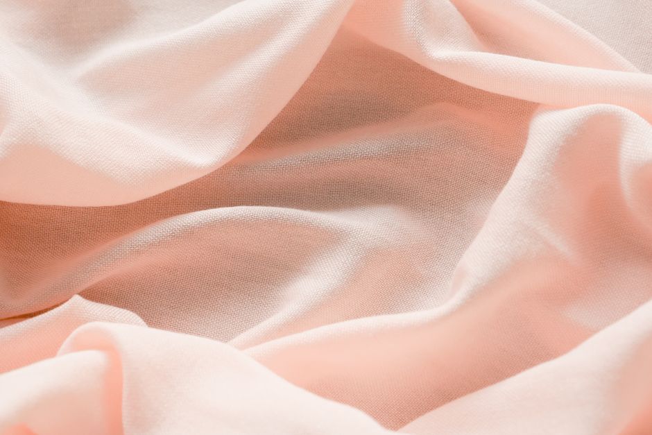 Close-up of pastel pink fabric with flowing folds, conveying softness and elegance.