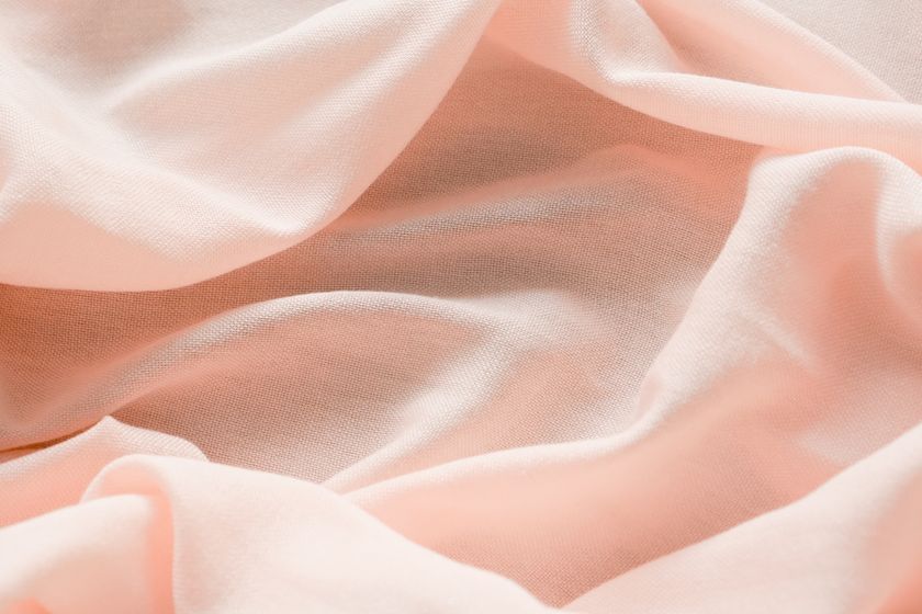 Close-up of a fine pale pink cloth gathered into soft close folds, light passing through the thinnest layers.