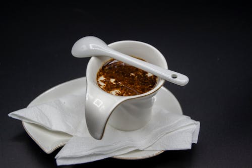 High angle of sauceboat with oil sauce placed on plate with napkin placed on black table