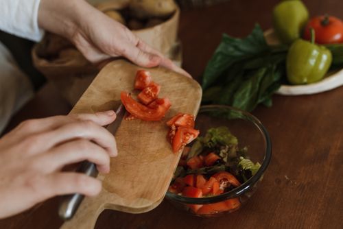 Free Close-up of hands chopping tomatoes on a wooden board for a healthy salad. Stock Photo