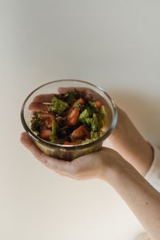A healthy green salad with tomatoes in a glass bowl, held by hands.