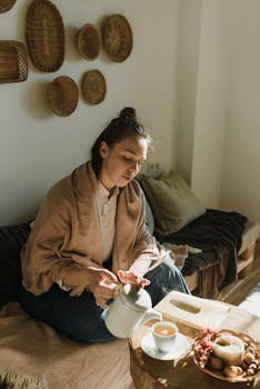 A woman enjoys a warm cup of tea in a sunlit room, wrapped in a cozy shawl.