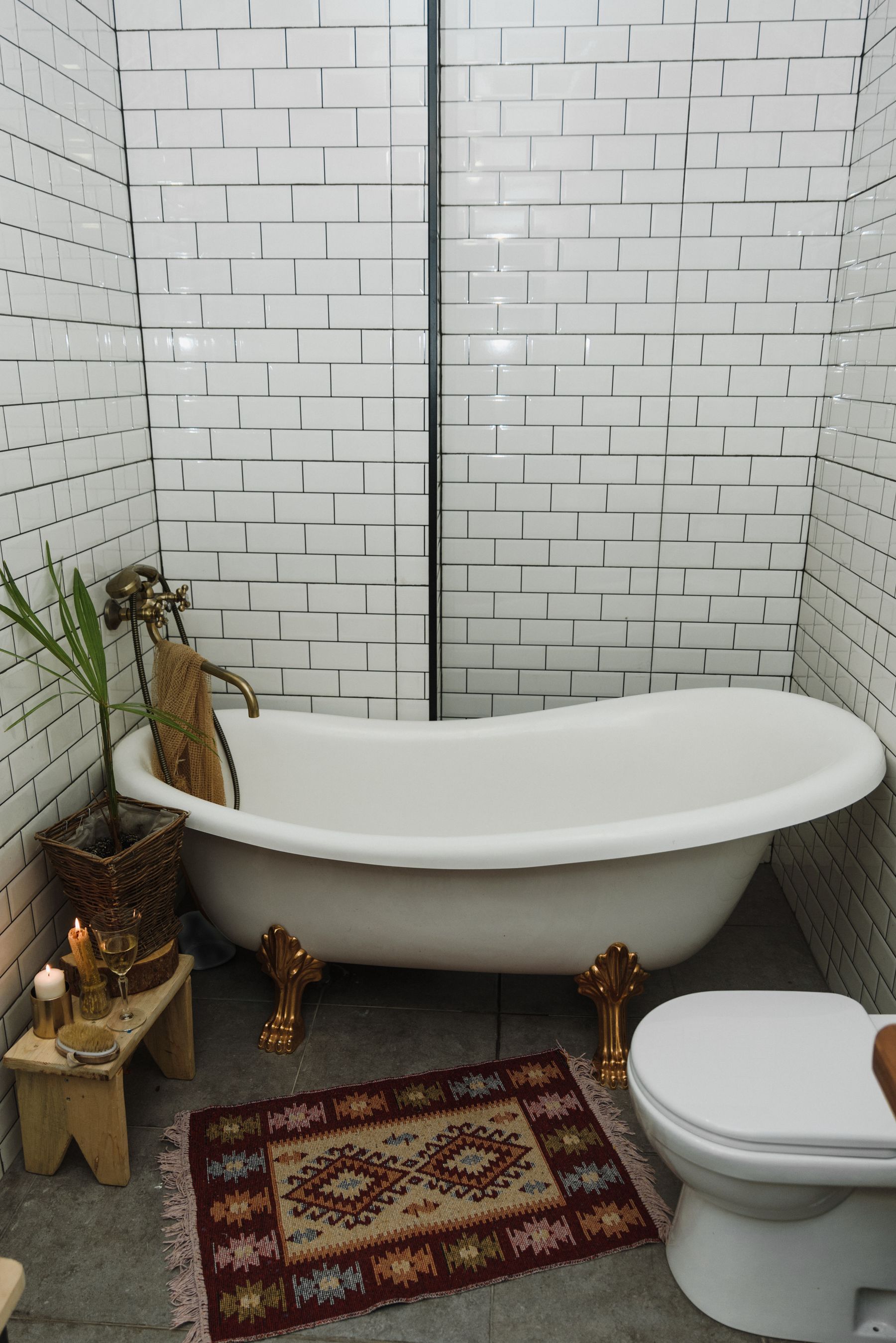 White clawfoot bathtub with warm rug, wood stool and soft decorative details