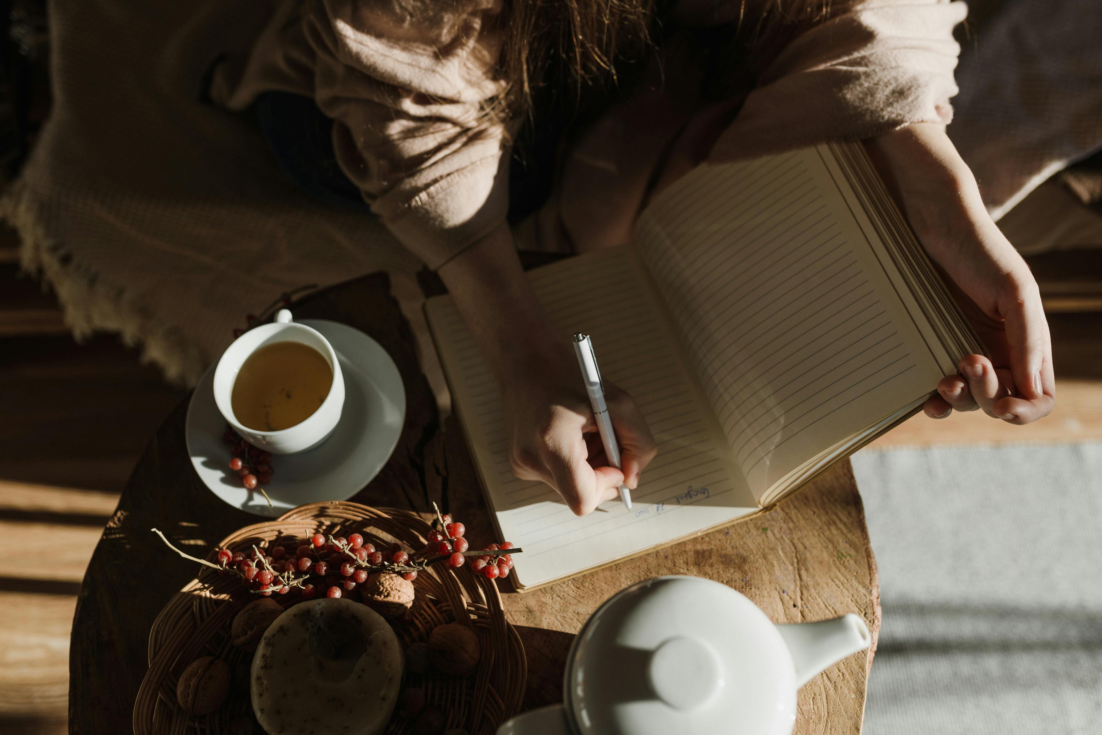 A peaceful scene of a person writing notes in a cozy setting with tea.