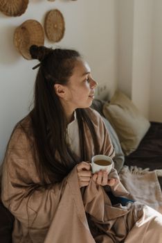 Woman enjoying a warm beverage while wrapped in a robe, creating a cozy atmosphere indoors.