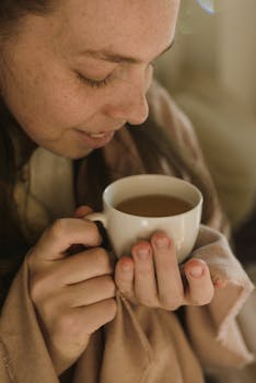 Close-up of a woman holding and smelling a coffee mug, capturing a cozy and relaxing moment.