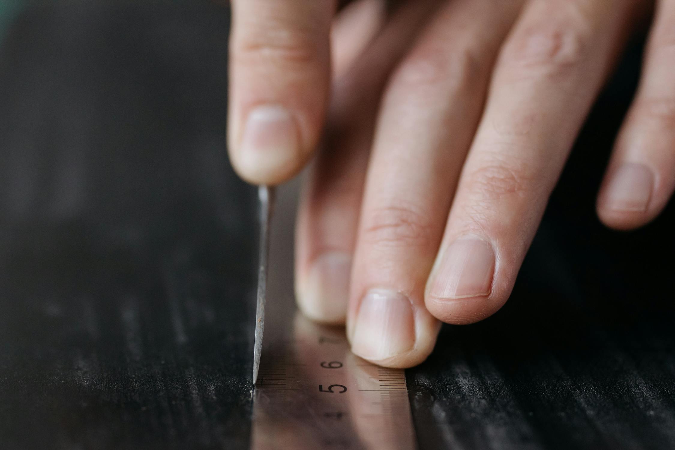A Person Marking a Black Material with a Stainless Steel Tool