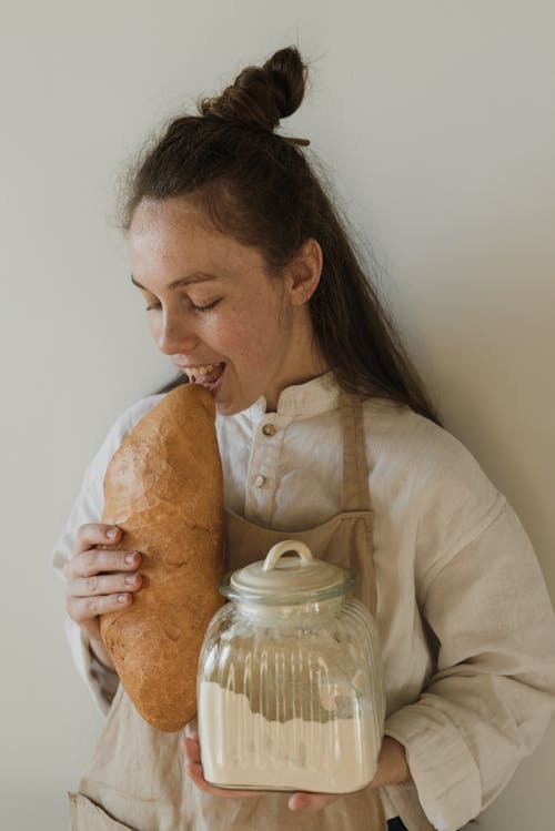 A Woman Holding a Loaf of Bread and a Jar of Flour