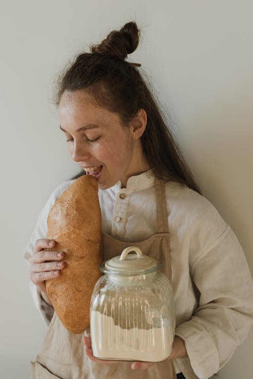 Free A Woman Holding a Loaf of Bread and a Jar of Flour Stock Photo