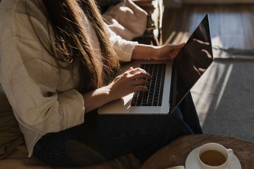 Free Close-up of a woman using a laptop in a warm, cozy indoor setting with sunlight. Stock Photo