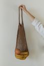 A Person Holding Brown Crocheted Bag with Bananas and Mandarin Fruit