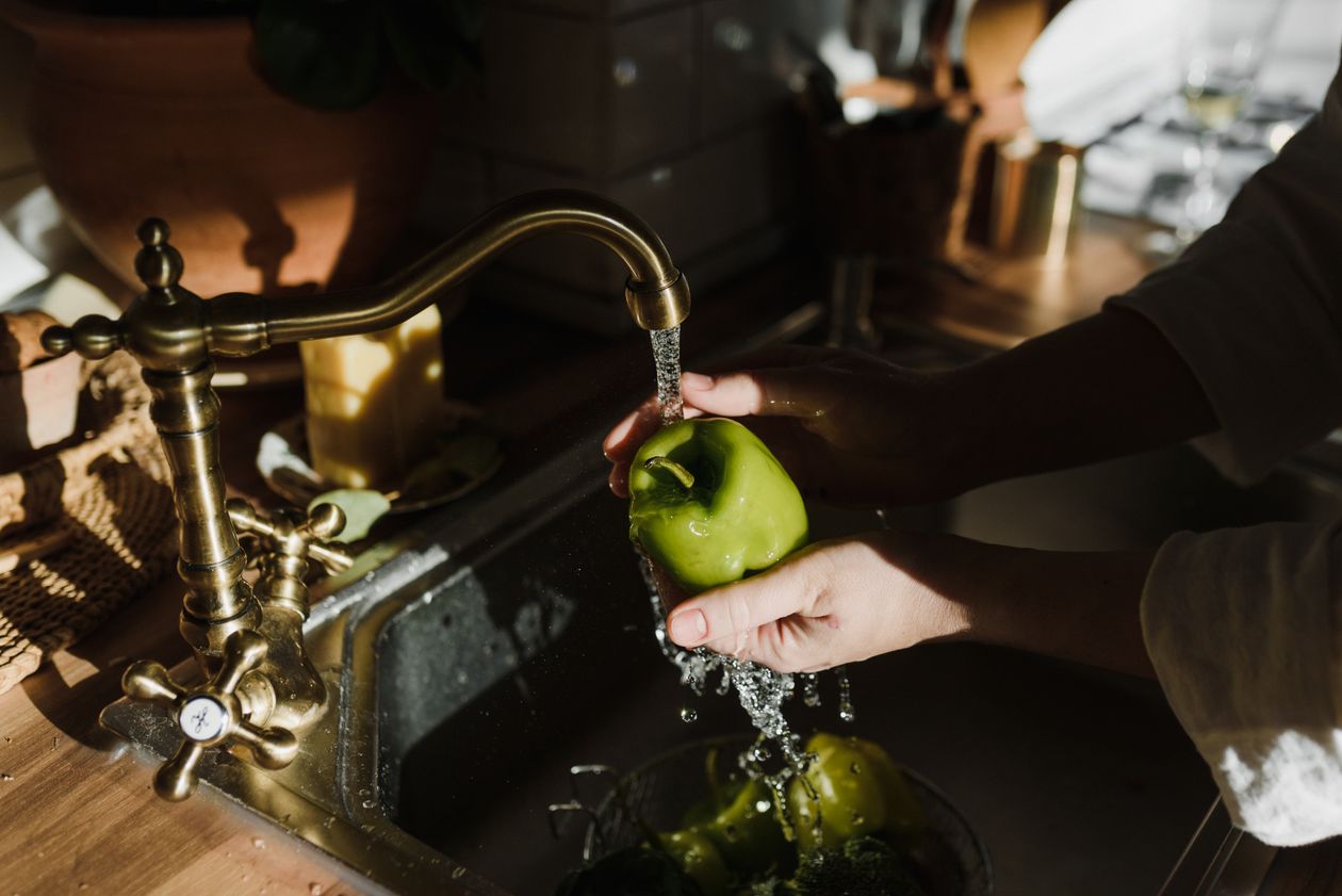Hands washing a pepper under a brass faucet