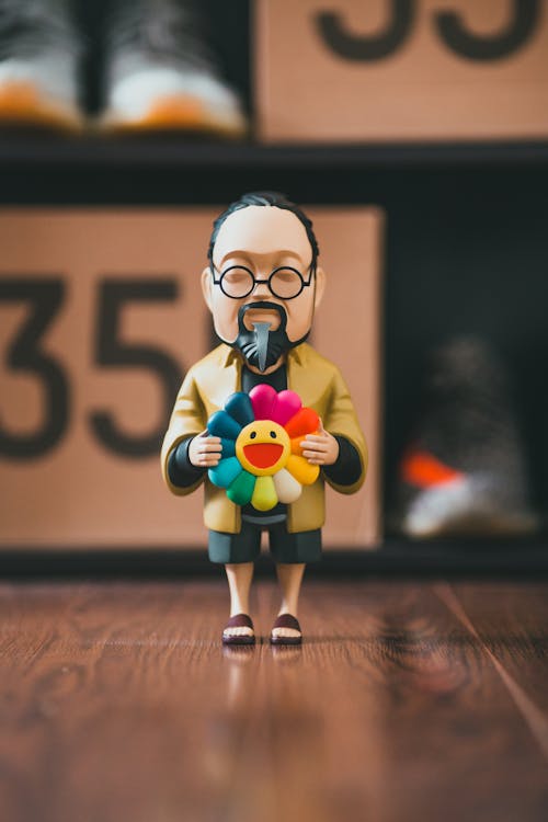 Free Miniature figurine of Asian male in glasses holding colorful flower placed on floor near shelf with shoe boxes Stock Photo