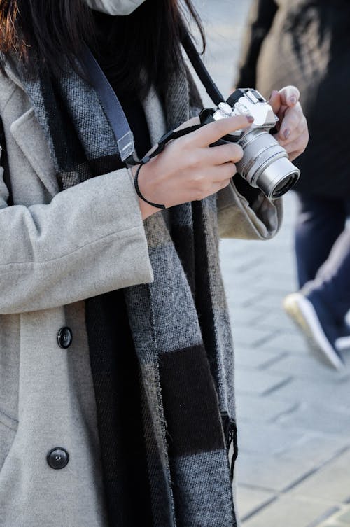Crop anonymous female in trendy warm clothes checking retro photo camera in daytime